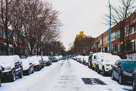 Snow Covered Road and Inline Parked Vehicles Between 2-storey Buildings Under White Sky